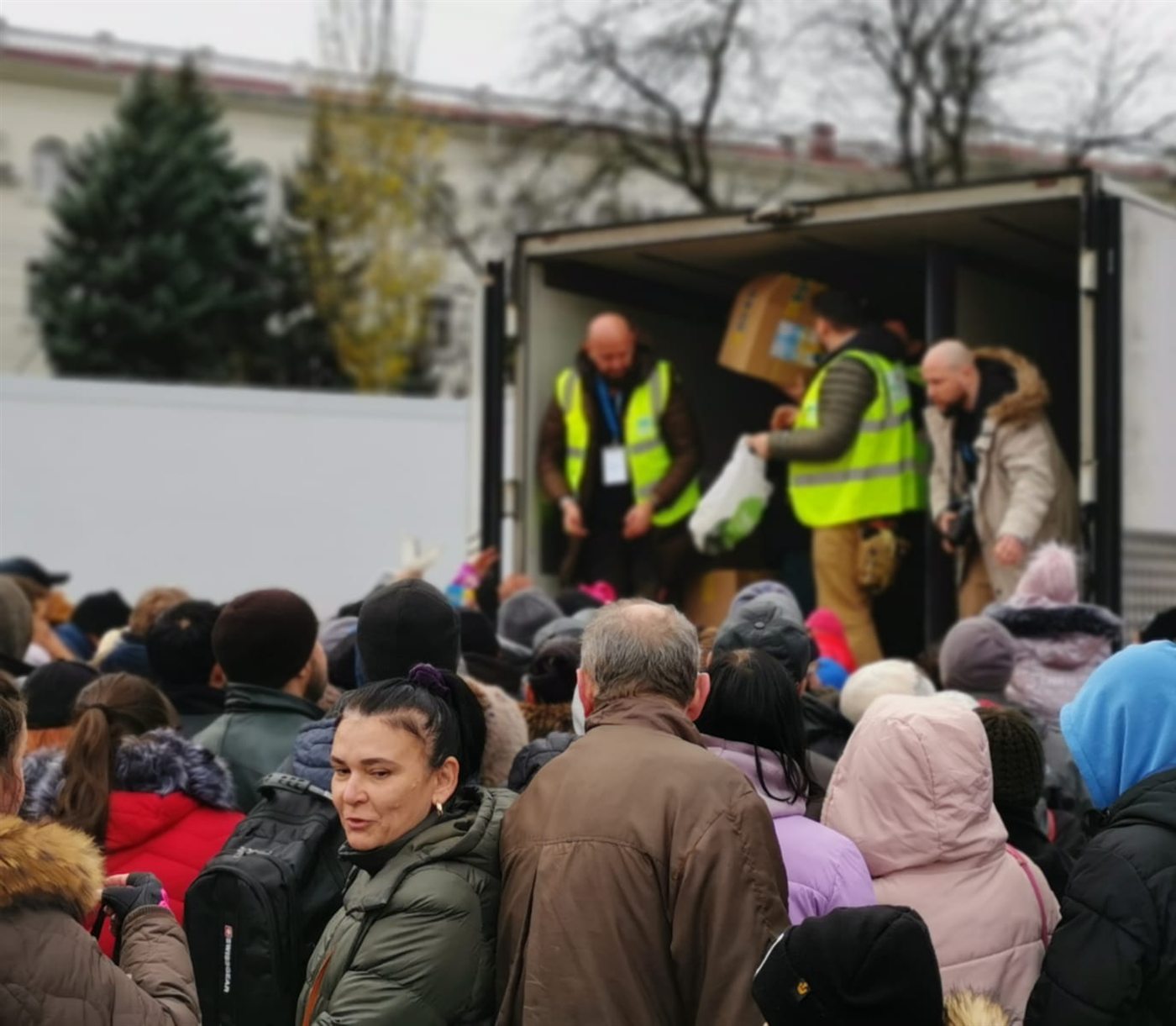 Волонтери у світловідбивних жилетах видають пакунки з гуманітарною допомогою з кузова фургона, поруч черга людей